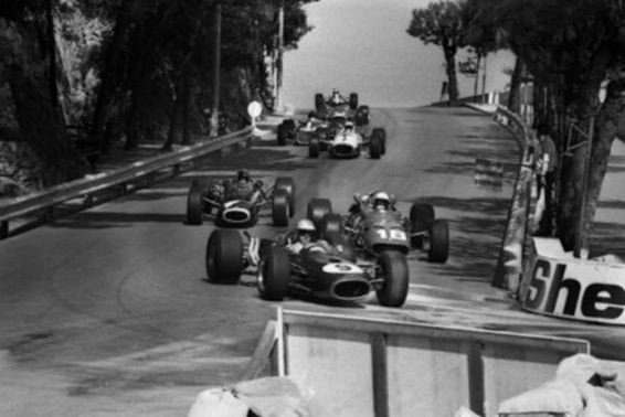 Le tournant de la course : Hulme passe Bandini au freinage de la chicane. On devine, en bas et à droite, la piste couverte de poudre de ciment pour absorber l’huile. Le passage des voitures va provoquer un tel nuage de poudre blanche que Jim Clark (que l’on voit ici tout en haut de la côte, en 7ème position), persuadé qu’il y a un carambolage, décide de prendre l’échappatoire @ DR (source : http//:formulapassion.it).